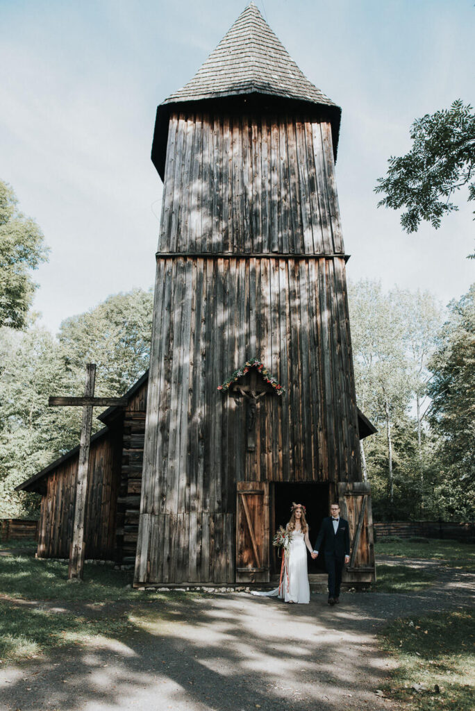 Para młoda pozuje na tle starego kościoła w Muzeum Wsi Opolskiej