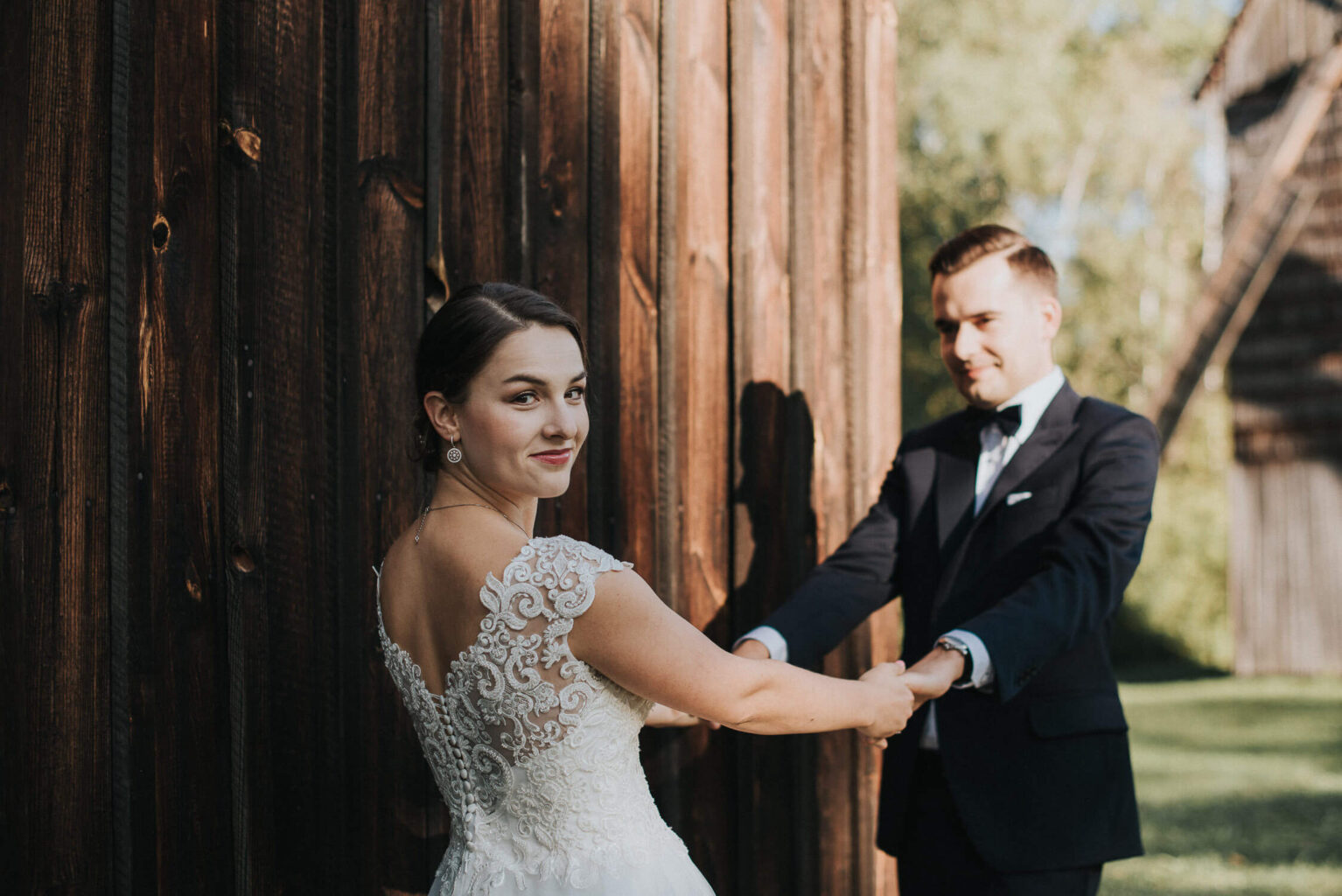 Państwo młodzi pozują na tle ściany starego kościoła w muzeum wsi opolskiej